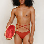 This gender-neutral, non binary Venus eco striped bikini bottom in terracotta red is shown from the front in the campaign.