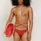 This gender-neutral, non binary Venus eco striped bikini bottom in terracotta red is shown from the front in the campaign.