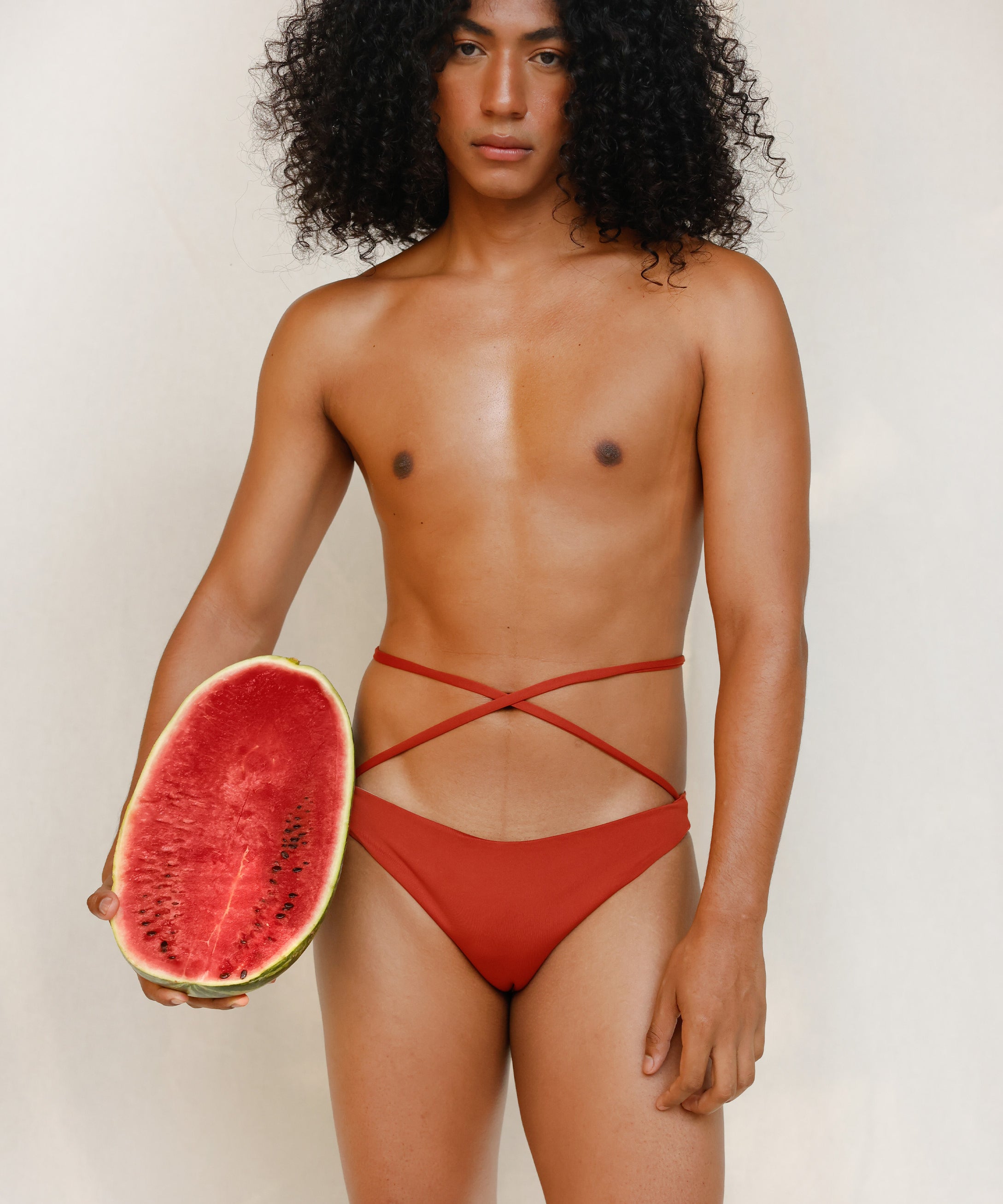 This gender-neutral, non binary Venus eco striped bikini bottom in terracotta red is shown from the front in the campaign.