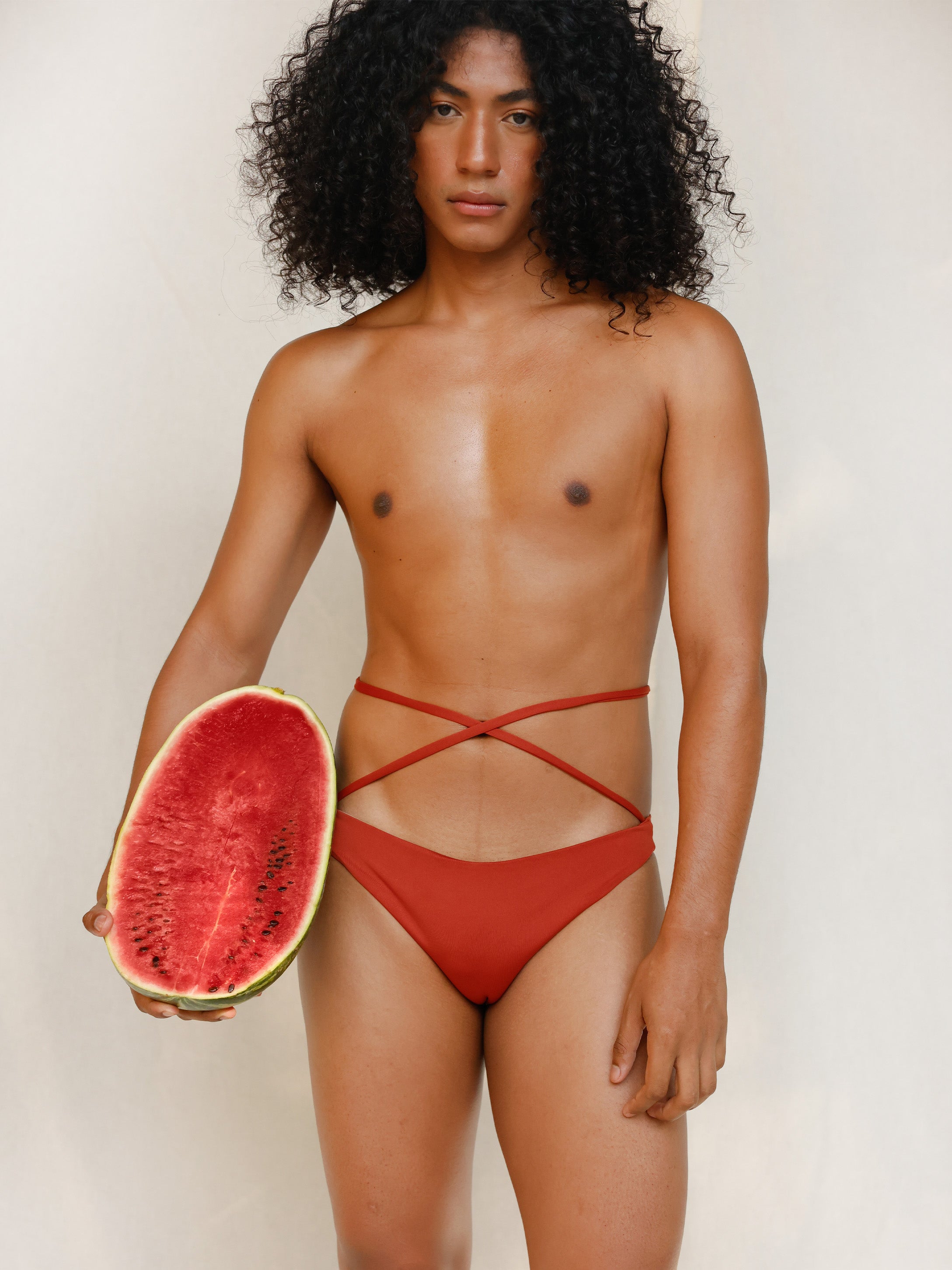 This gender-neutral, non binary Venus eco striped bikini bottom in terracotta red is shown from the front in the campaign.