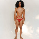 This bikini bottom is a gender-neutral, nonbinary Venus eco striped design in terracotta red, shown from the front. 