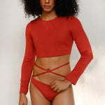 the model is wearing the Doris long-sleeve swim crop top rashguard in terracotta red paired with the Venus striped bikini bottom, a gender-neutral, nonbinary sustainable swimwear set with a soft, modern fit.