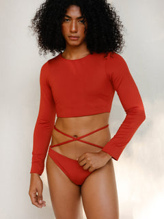 the model is wearing the Doris long-sleeve swim crop top rashguard in terracotta red paired with the Venus striped bikini bottom, a gender-neutral, nonbinary sustainable swimwear set with a soft, modern fit.