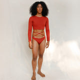 The model is wearing the Doris long-sleeve swim crop top rashguard in terracotta red, paired with the Venus striped terracotta red bikini bottom, it is highlighting the sustainable design and gender-neutral, nonbinary fit.