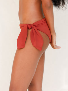 Side view of model in Coris bikini bottom, terracotta red. Gender neutral, gender-affirming, inclusive and sustainable.