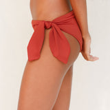 Side view of model in Sylvia bikini bottom, terracotta red 