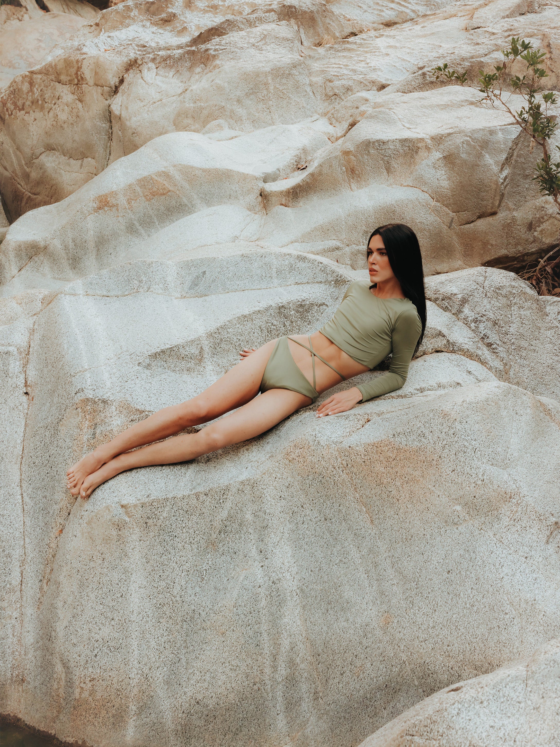A model is shown from the front wearing the Doris long-sleeve sustainable swim crop top rashguard in mineral green with the Venus striped bikini bottom, a gender-neutral, nonbinary swimwear set with a sleek, modern look.
