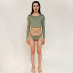 Model wears the Doris long-sleeve swim crop top rashguard in mineral green. It is paired with the Venus striped bikini bottom, a gender-neutral, nonbinary sustainable set shown from the front.