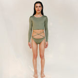 Model wears the Doris long-sleeve swim crop top rashguard in mineral green. It is paired with the Venus striped bikini bottom, a gender-neutral, nonbinary sustainable set shown from the front.