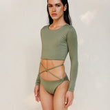 The model is wearing the Doris long-sleeve swim crop top rashguard in mineral green with the Venus striped bikini bottom, shown from the side as a gender-neutral, nonbinary sustainable swimwear set.