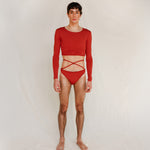 The model wears the Doris long-sleeve swim crop top rashguard in terracotta red with the Venus striped bikini bottom, a gender-neutral, nonbinary swimwear look shown from the front.