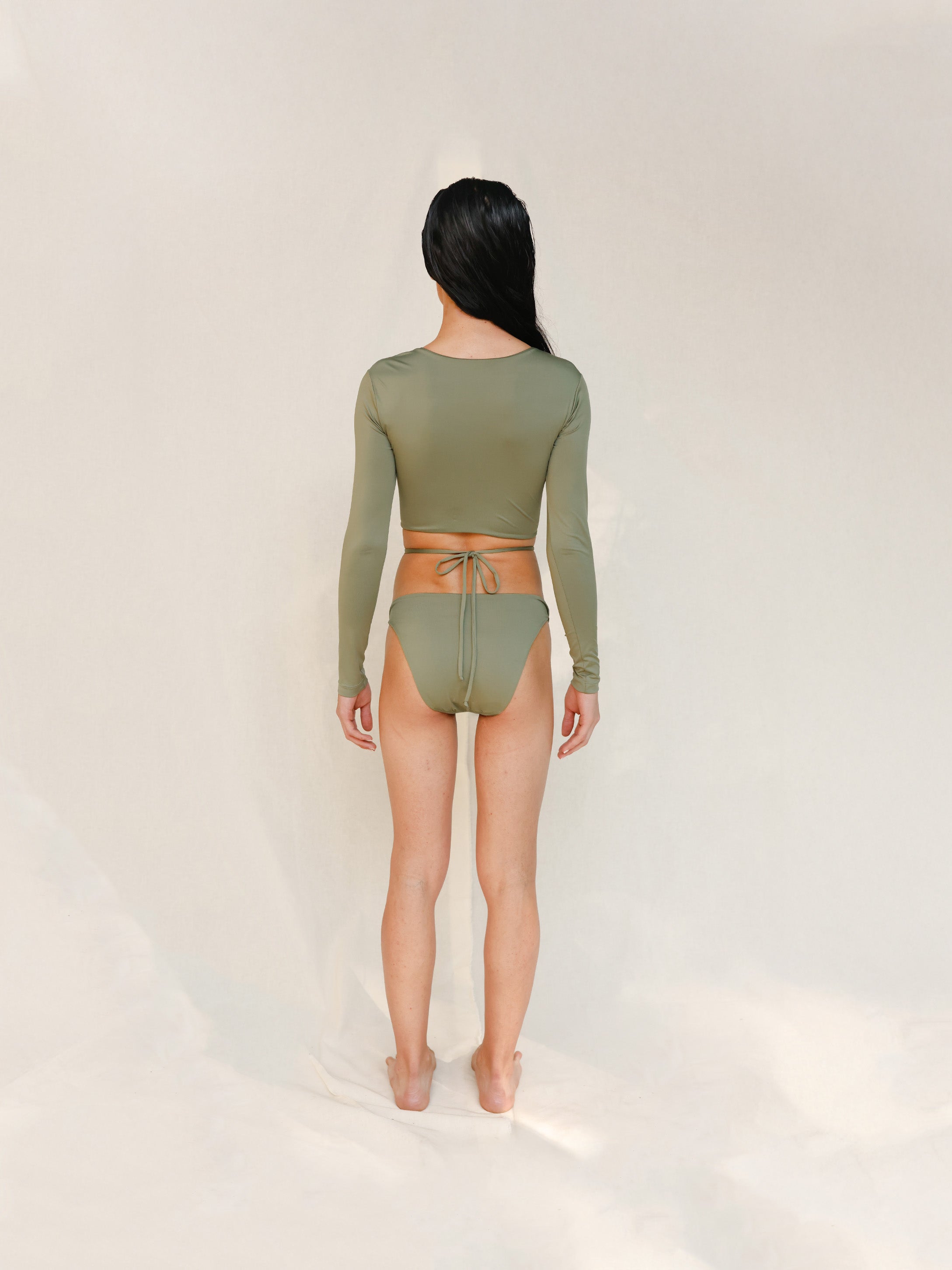 this picture is showcasing back view of the Doris long-sleeve swim crop top rashguard in mineral green paired paired with the Venus striped bikini bottom.it's a gender-neutral, nonbinary sustainable swimwear set with a clean, modern silhouette.