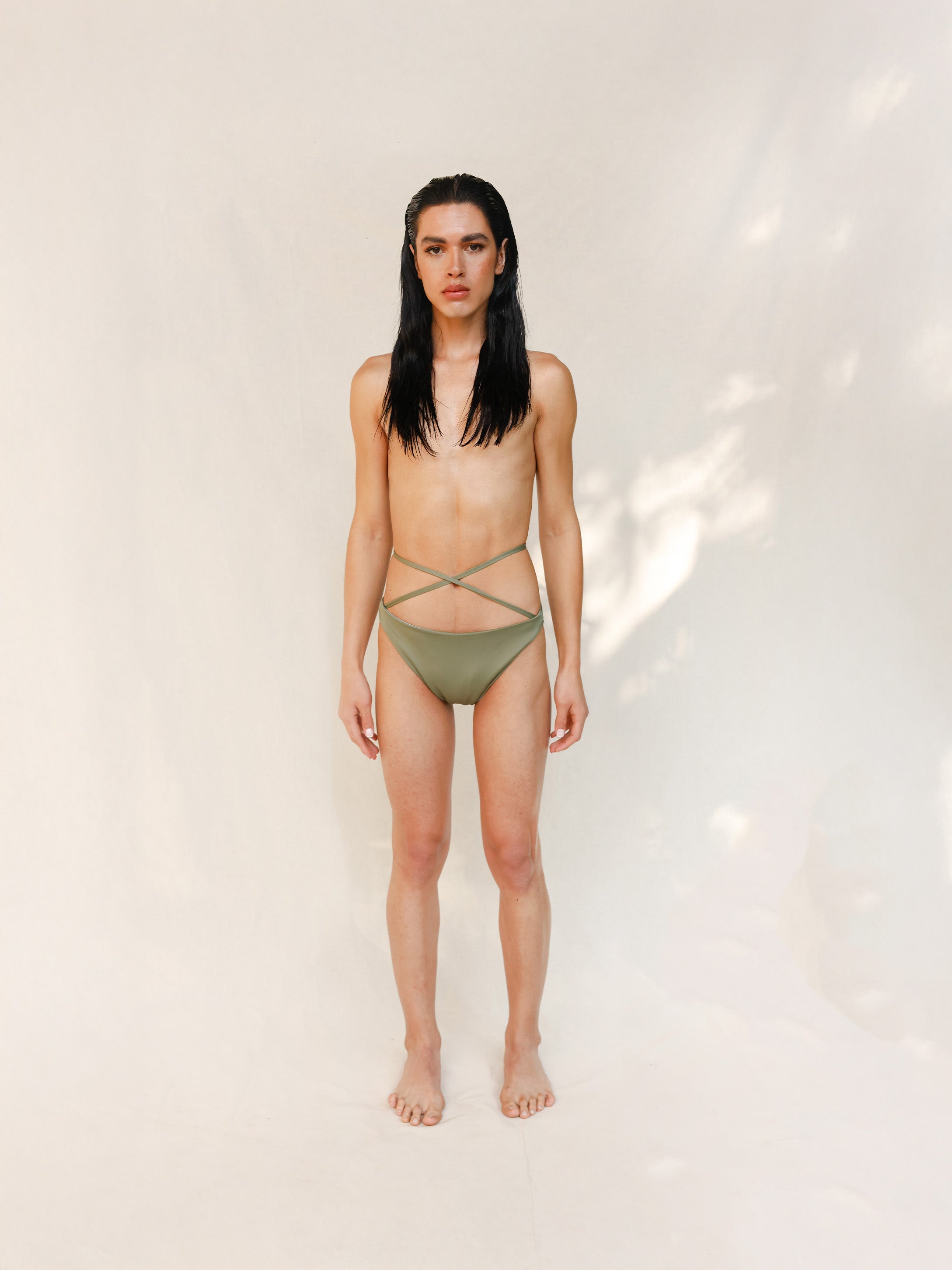 Model is wearing the Venus eco striped bikini bottom in mineral green which is a gender-neutral, nonbinary sustainable design shown from the front. it has a clean, minimal fit.
