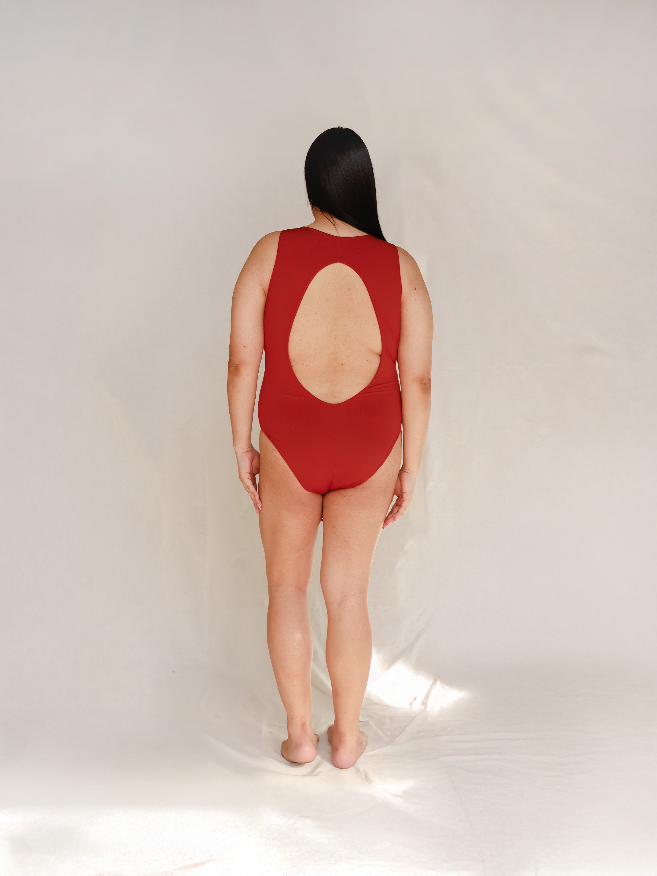 Person wearing Marsha one-piece swimsuit in terracotta red, back view