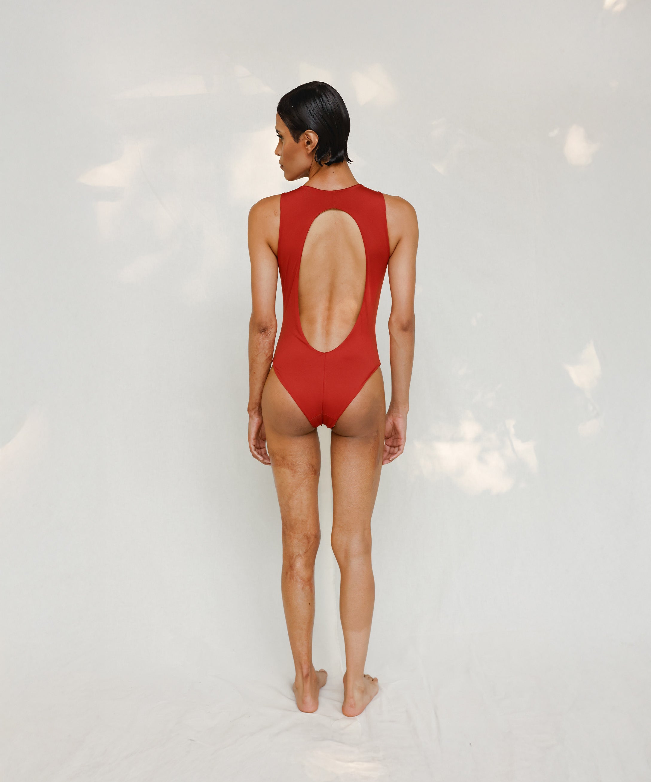Person wearing Marsha one-piece swimsuit in terracotta red, back view