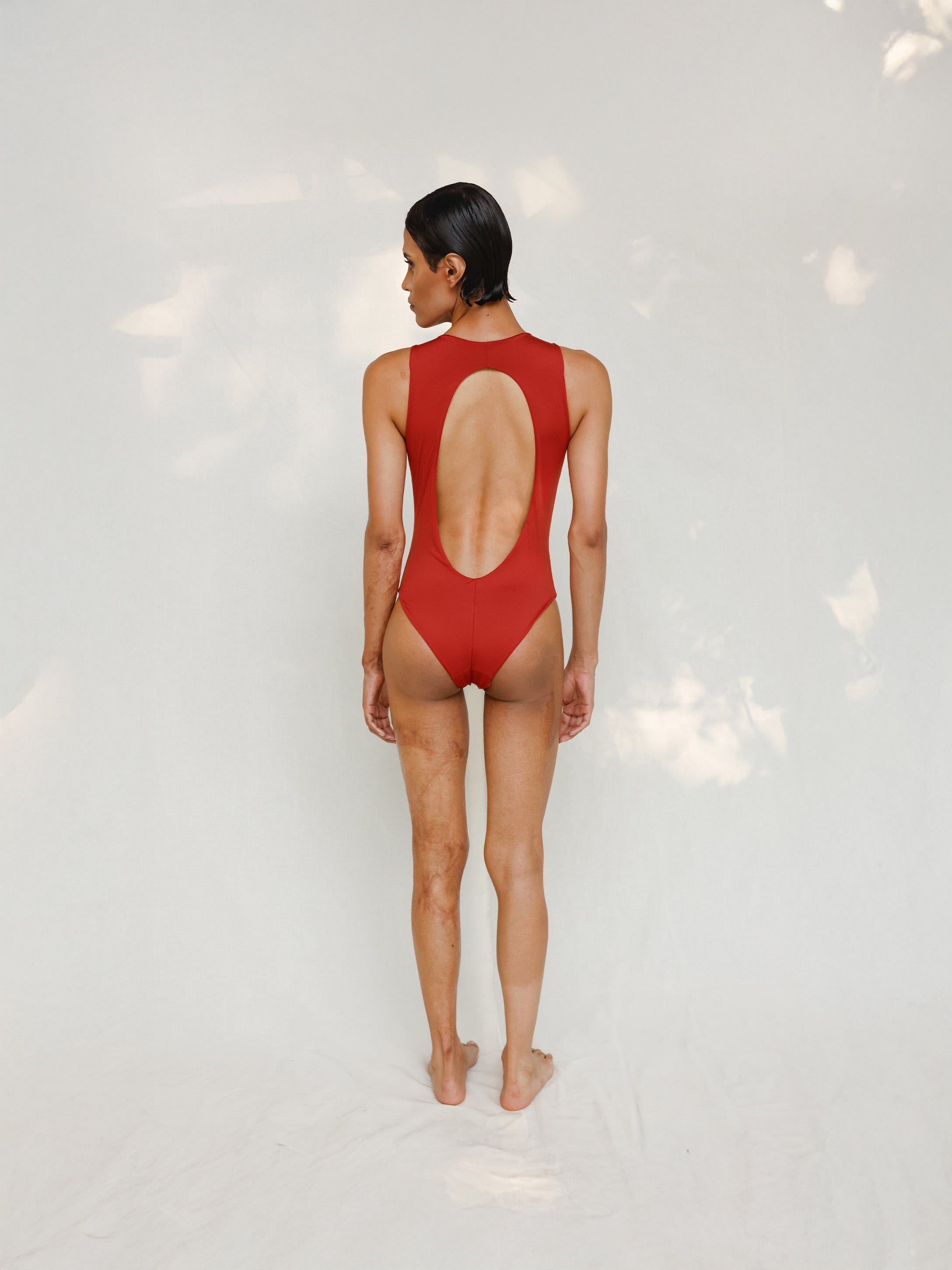 Person wearing Marsha one-piece swimsuit in terracotta red, back view